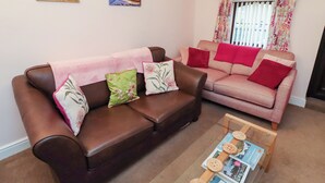 Ein Wohnzimmer mit zwei Sofas, einem Couchtisch mit Zeitschriften und zwei Bildern an der Wand.