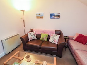 Un salon avec un canapé en cuir marron, une table basse en verre et un lampadaire. Deux tableaux sont accrochés au mur.