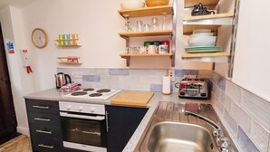 Eine Küche mit Herd, Backofen, Spüle und verschiedenen Küchenutensilien auf Regalen.