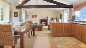 Una cocina amplia con vigas de madera, un comedor con sillas de mimbre y una chimenea.