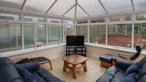 A conservatory with a TV, sofas, and a wooden table.