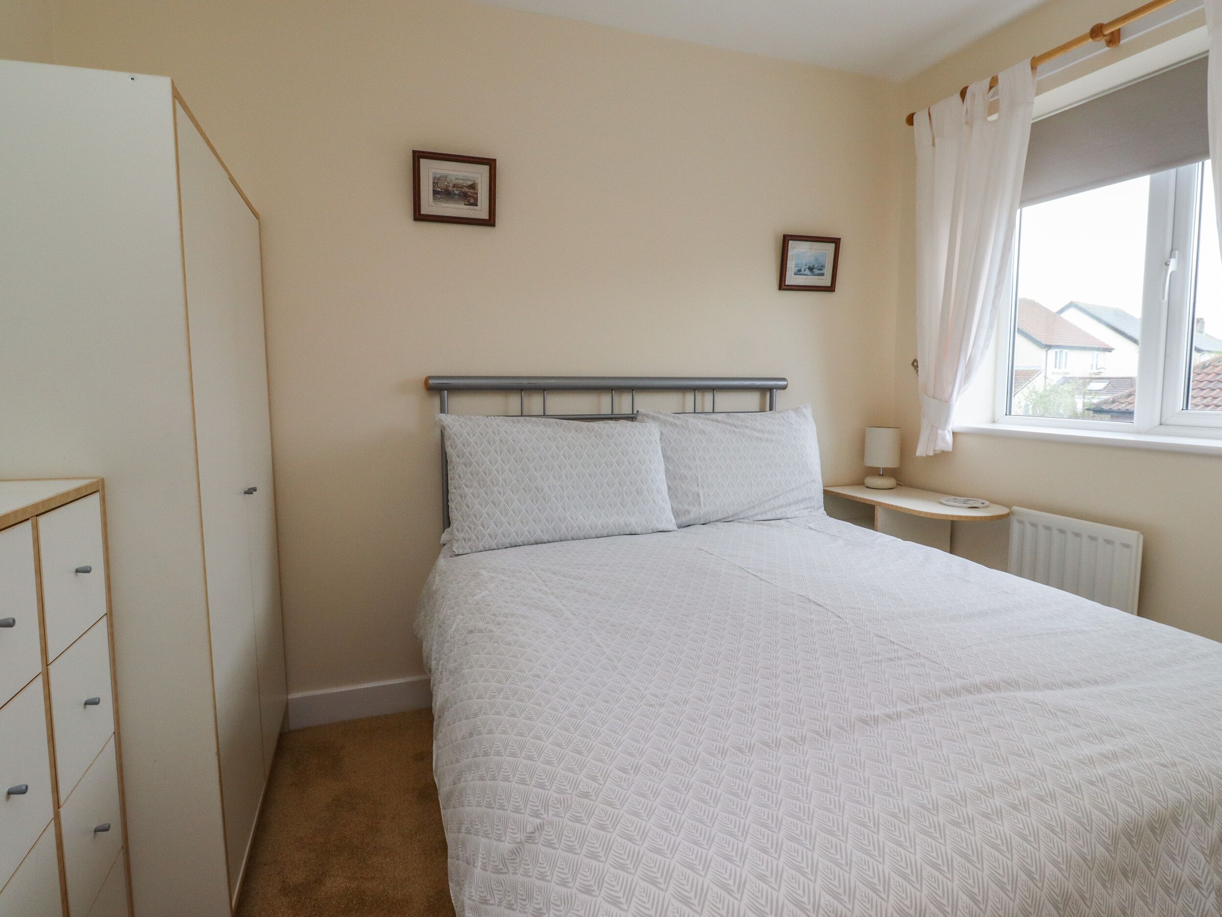 A bedroom with a bed, a nightstand, a dresser, and a window with curtains.