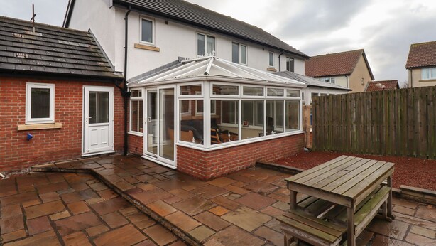 A house with a conservatory, a brick exterior, and a tiled patio.
