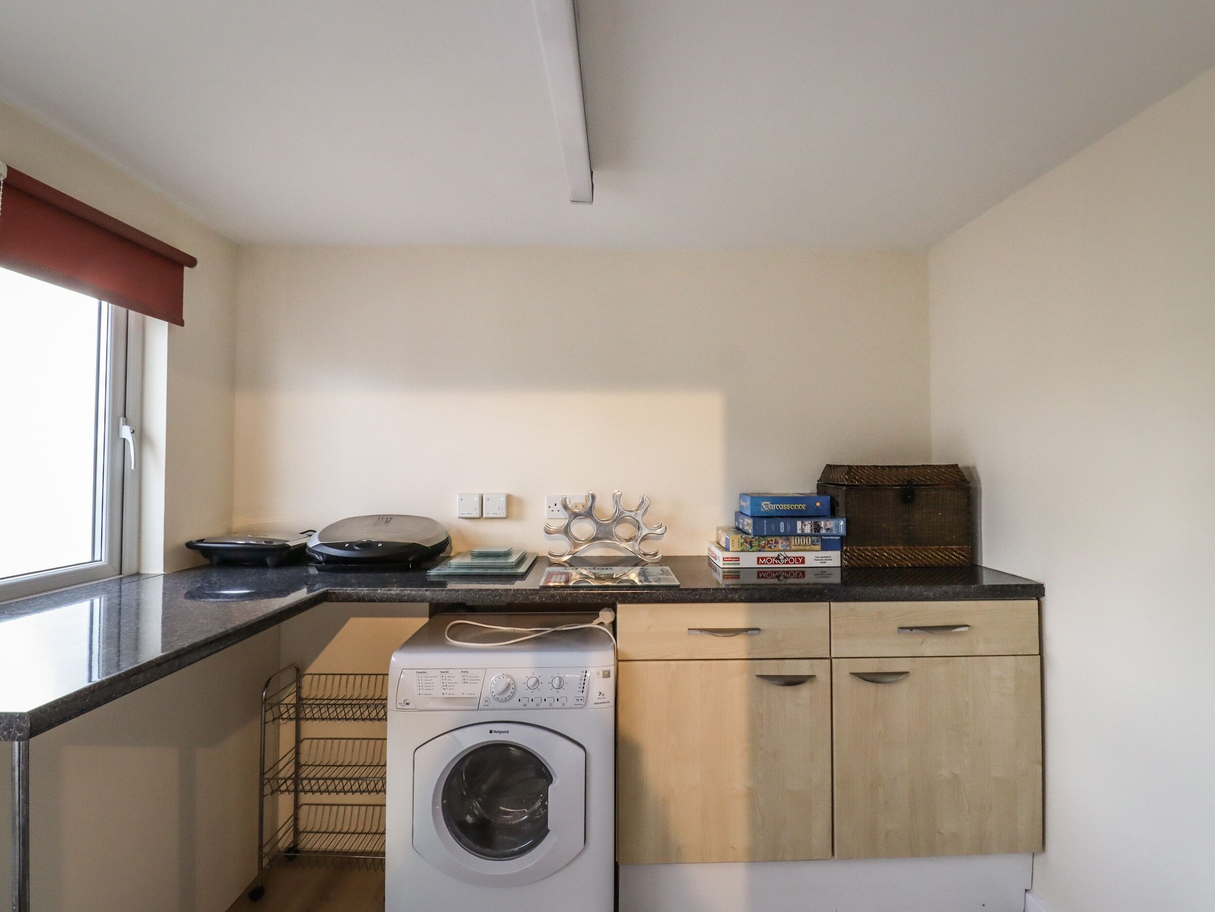 A compact laundry room with a front-loading washing machine, a drying rack, and a small countertop with board games.