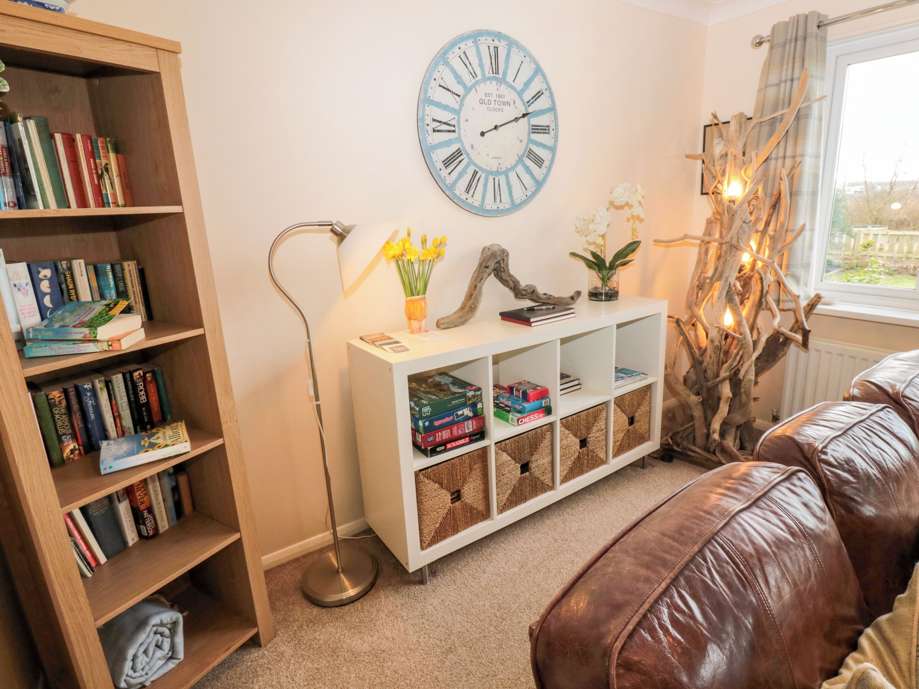 A cozy living room with a bookshelf, a white console table with chess sets, a clock, and a brown leather couch.
