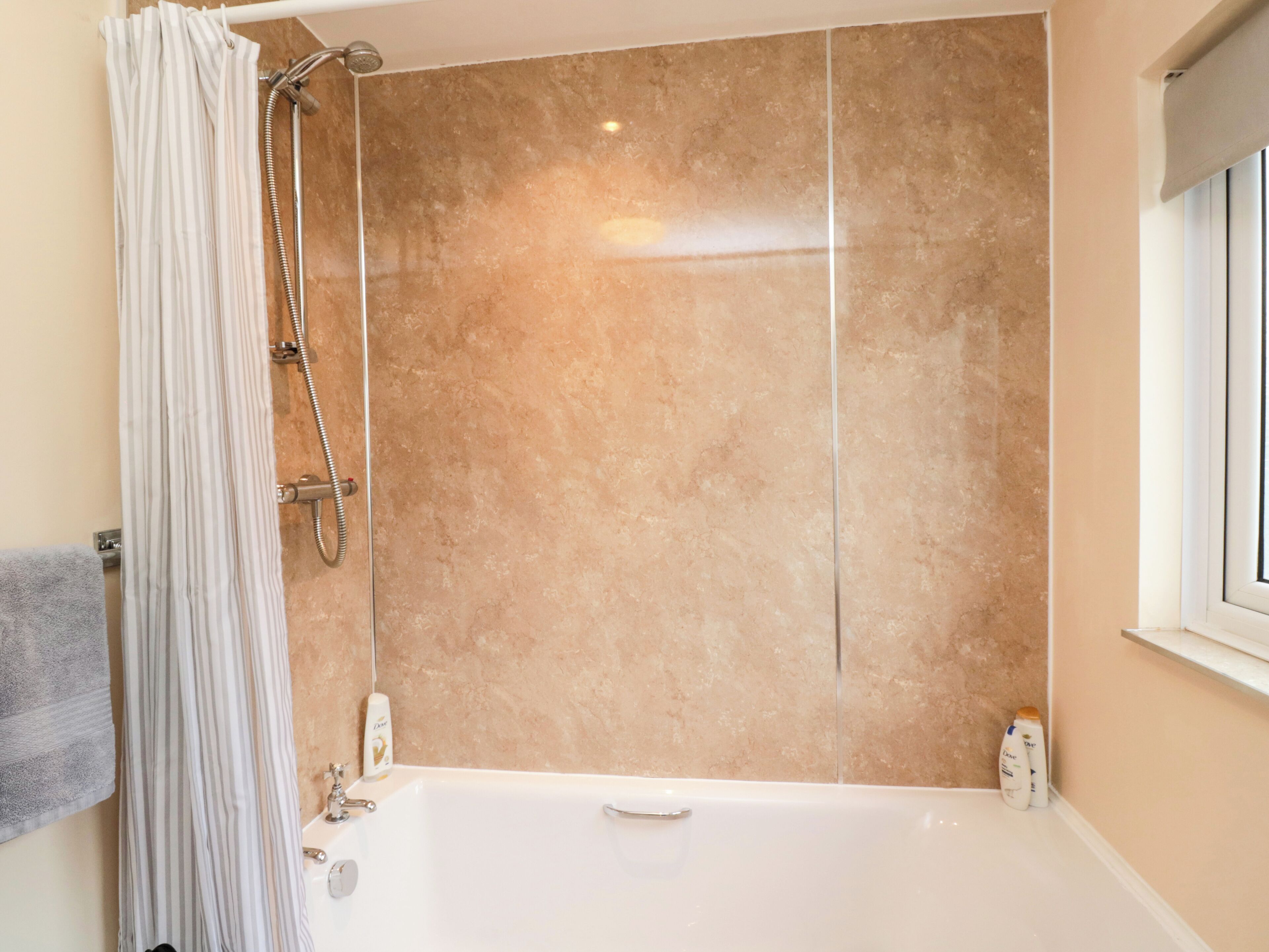 A bathroom with a bathtub, shower, and beige tiled walls.