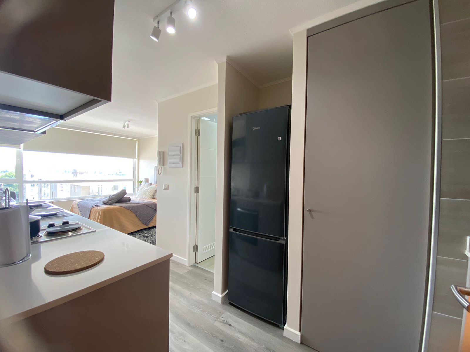 Una cocina moderna con refrigerador, un comedor con mesa y sillas, y un dormitorio con cama y ventana.