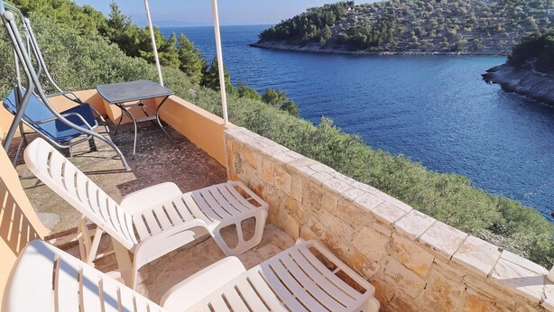 A terrace with white plastic chairs and a table overlooking a coastal area with a stone wall and a view of the sea. - Peaceful Holiday House Senija (Vela Luka)