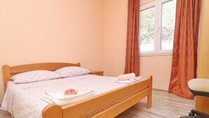 A neatly made bed with a floral bedspread and two pillows, a wooden nightstand with a lamp, and a window with curtains. - Peaceful Holiday House Senija (Vela Luka)