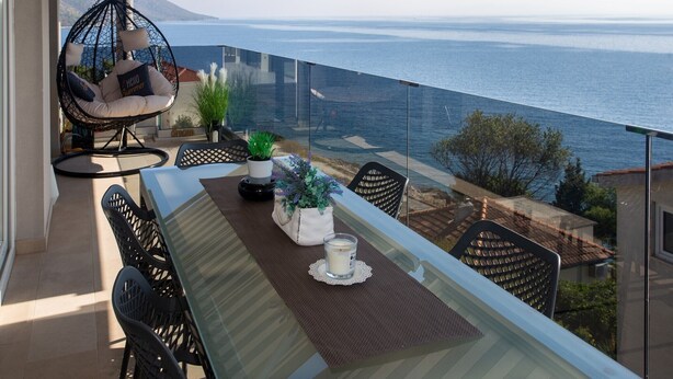 Un balcon avec une table en verre, des chaises, un fauteuil suspendu et une vue sur la mer.