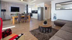 Un salon moderne avec un canapé, un coin repas comprenant une table et des chaises, une cuisine équipée d’un réfrigérateur et un grand miroir accroché au mur.