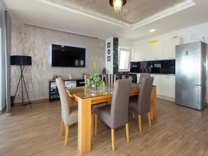 A modern kitchen with white cabinets, a stainless steel refrigerator, and a dining area with a wooden table and chairs.