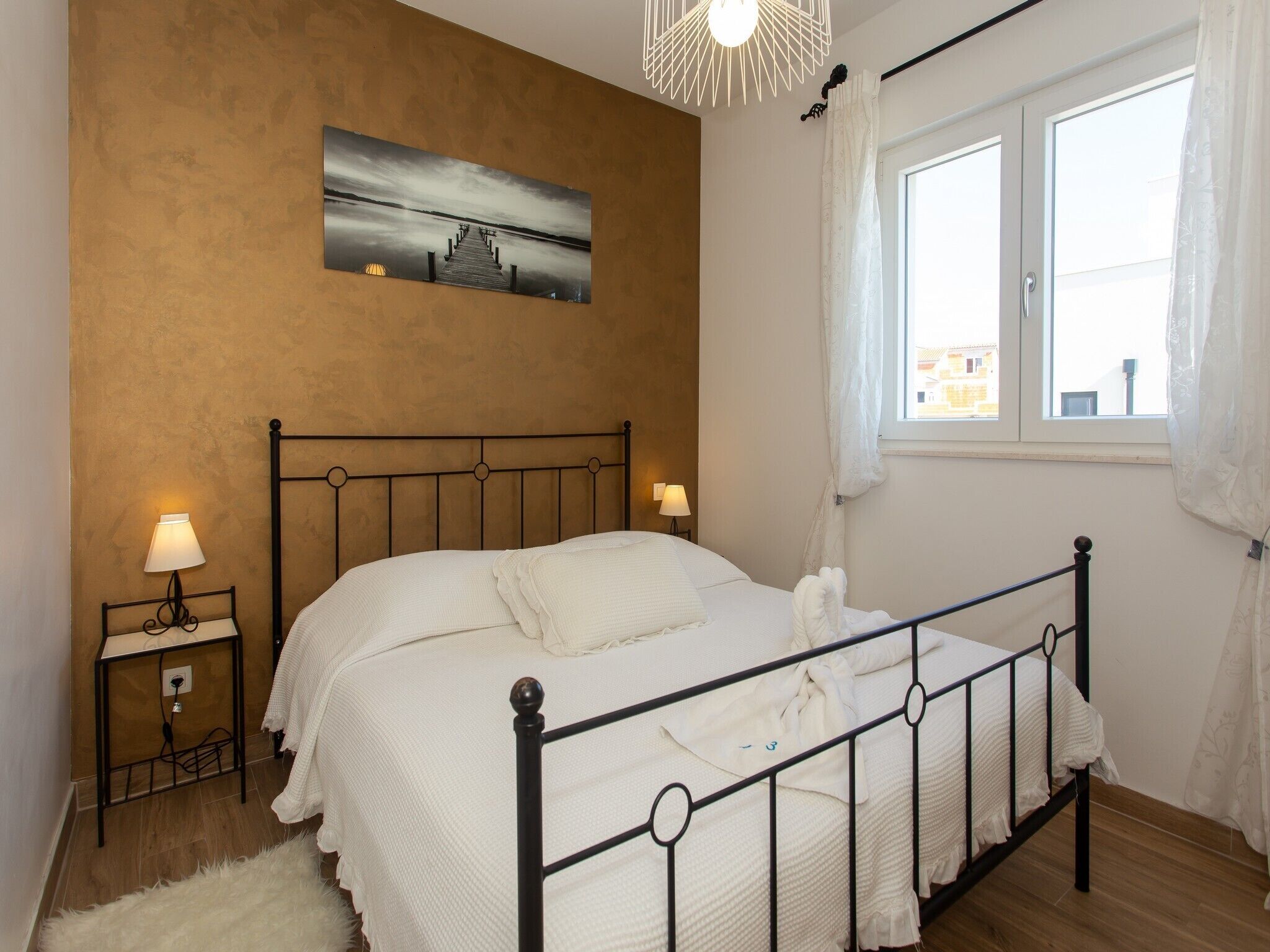 Un dormitorio con cama, dos mesitas de noche con lámparas, una ventana con cortinas y un cuadro en la pared.