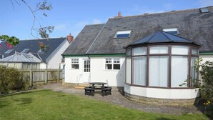 A house with a conservatory, a patio with a table and chairs, and a well-maintained lawn. - Armstrong Cottages No22 (Bamburgh)