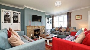 A living room with a fireplace, two sofas, a television, and a bookshelf. - Armstrong Cottages No22 (Bamburgh)