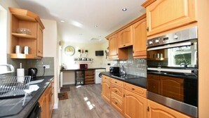 A modern kitchen with wooden cabinets, stainless steel appliances, and a black countertop. - Armstrong Cottages No22 (Bamburgh)