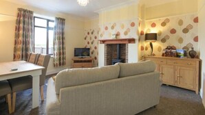 A cozy living room with a sofa, a dining table, a TV, and a fireplace. - Dairyman's Cottage (Morpeth)