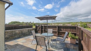 An outdoor patio with a round table and chairs, a large umbrella, and a wooden fence. - Dairyman's Cottage (Morpeth)