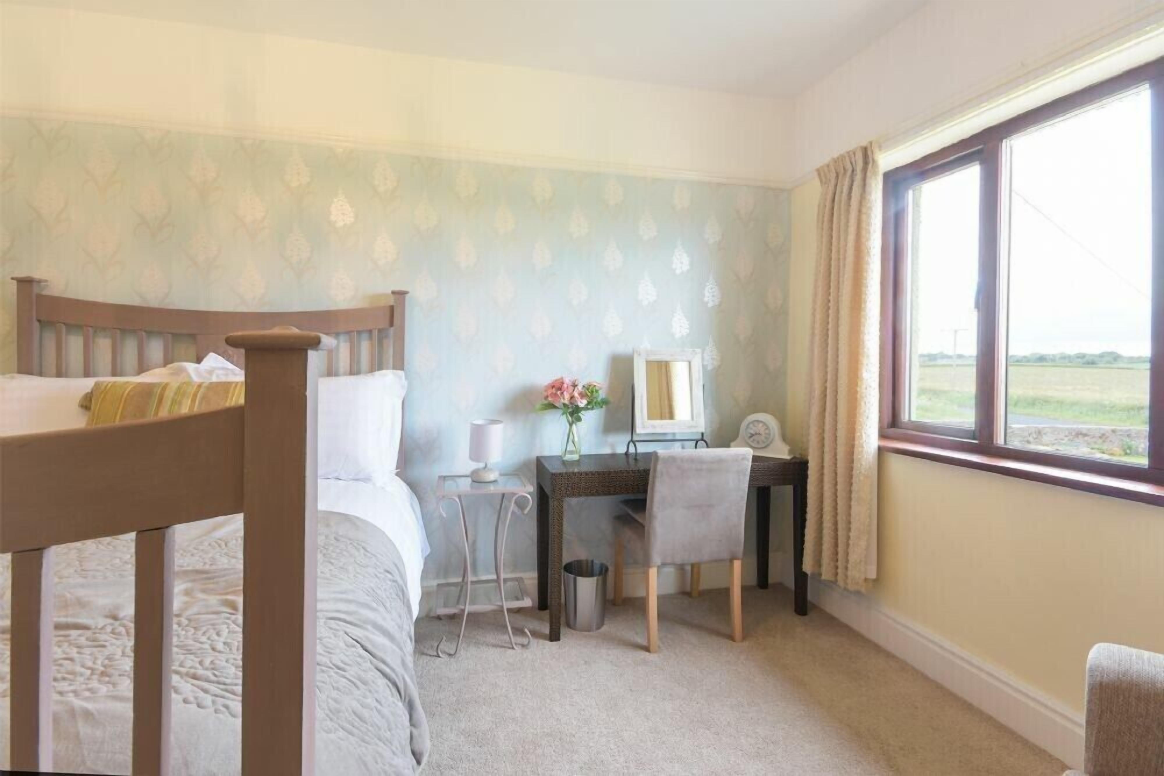 A bedroom with a bed, a desk, and a chair. There is a window with a view of the outdoors.