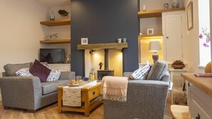 Een gezellige woonkamer met twee grijze banken, een houten salontafel, een open haard en een televisietoestel.