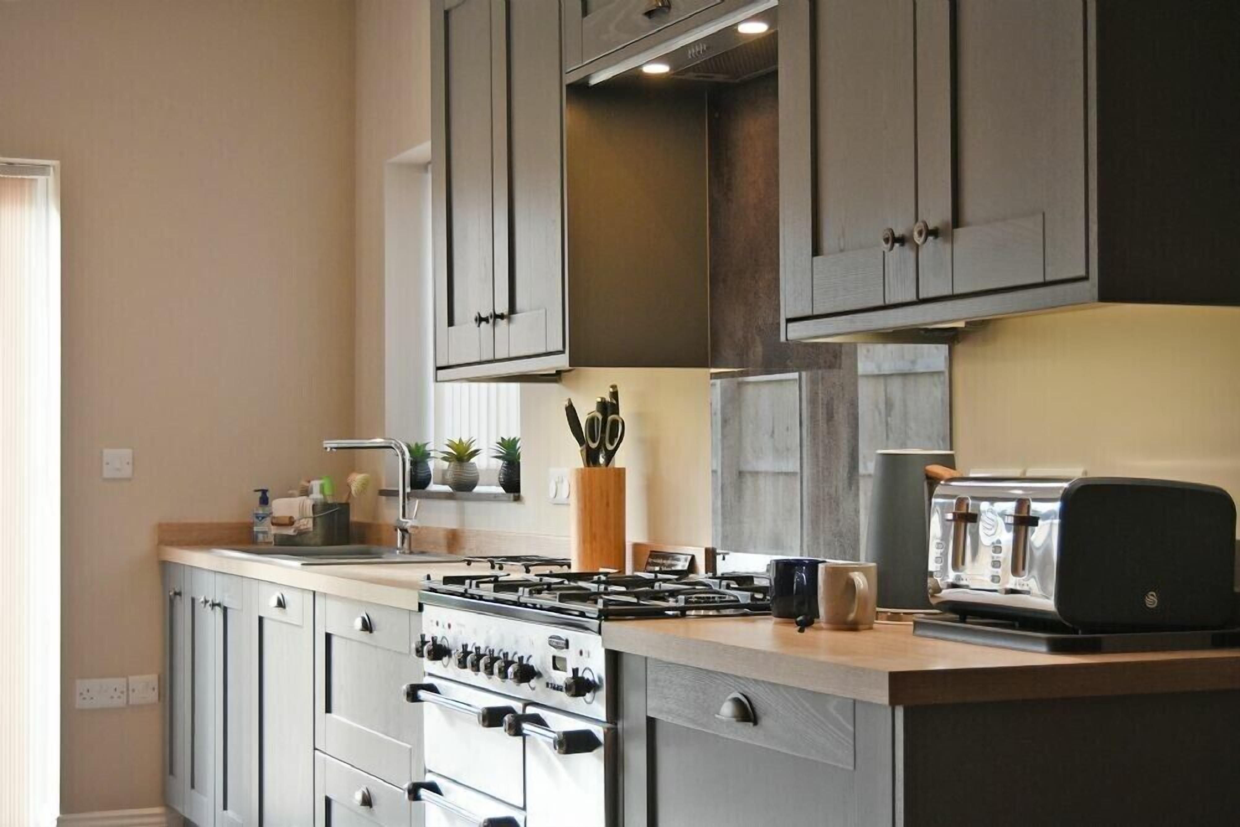 A modern kitchen with grey cabinets, a gas stove, a toaster, and a coffee maker.