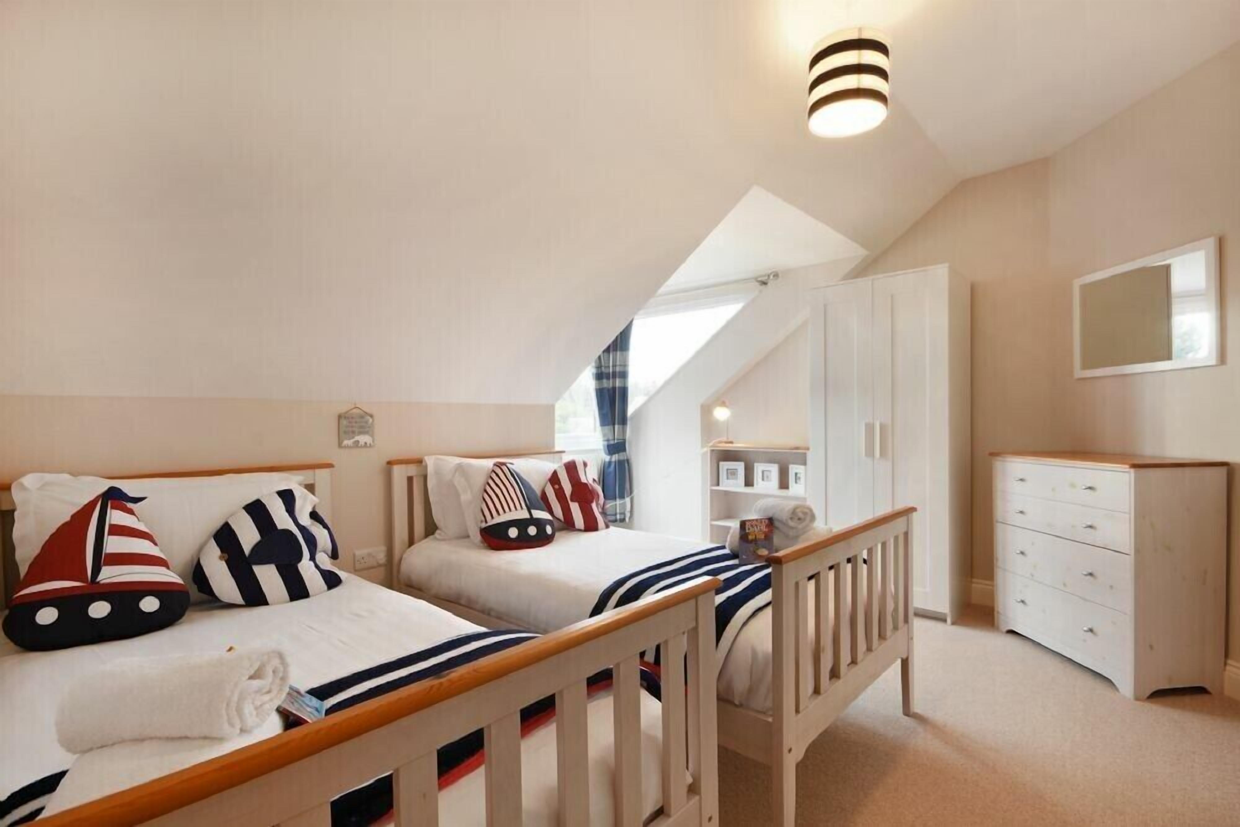 A bedroom with two beds, a wooden dresser, a white wardrobe, and a skylight.