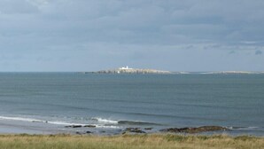 Un paysage côtier avec un phare sur une petite île, une mer calme et une plage herbeuse.