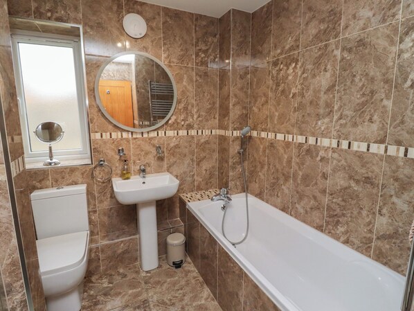 A bathroom with a toilet, sink, mirror, and bathtub. - Assisi Apartment (Alnwick)