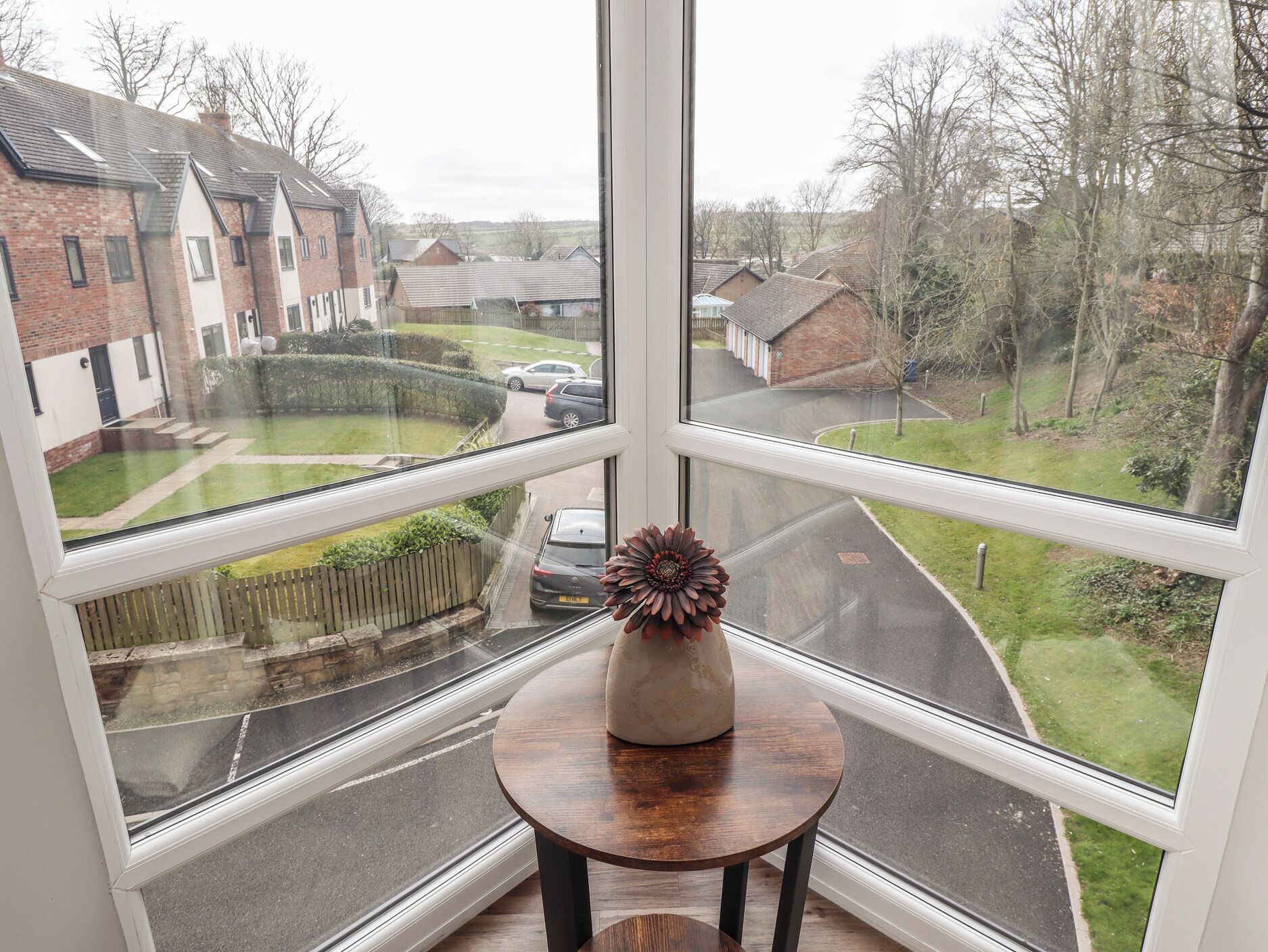 A room with a large window offering a view of a residential street and houses.