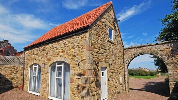A stone building with a red-tiled roof, arched windows, and a stone archway.