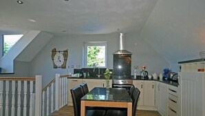 A modern kitchen with a dining area, featuring a large stove, a clock on the wall, and a window providing natural light.