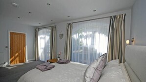 A bedroom with a large bed, curtains, a wooden door, and a small table with a vase.