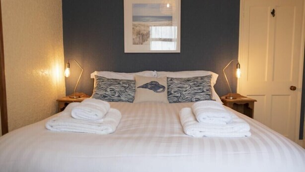 Una cama bien hecha con sábanas blancas y dos almohadas, un cuadro en la pared y dos lámparas de noche.