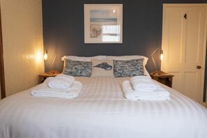 A neatly made bed with white linens and two pillows, a framed picture on the wall, and two bedside lamps. - Kittiwake Cottage, Seahouses (Seahouses)