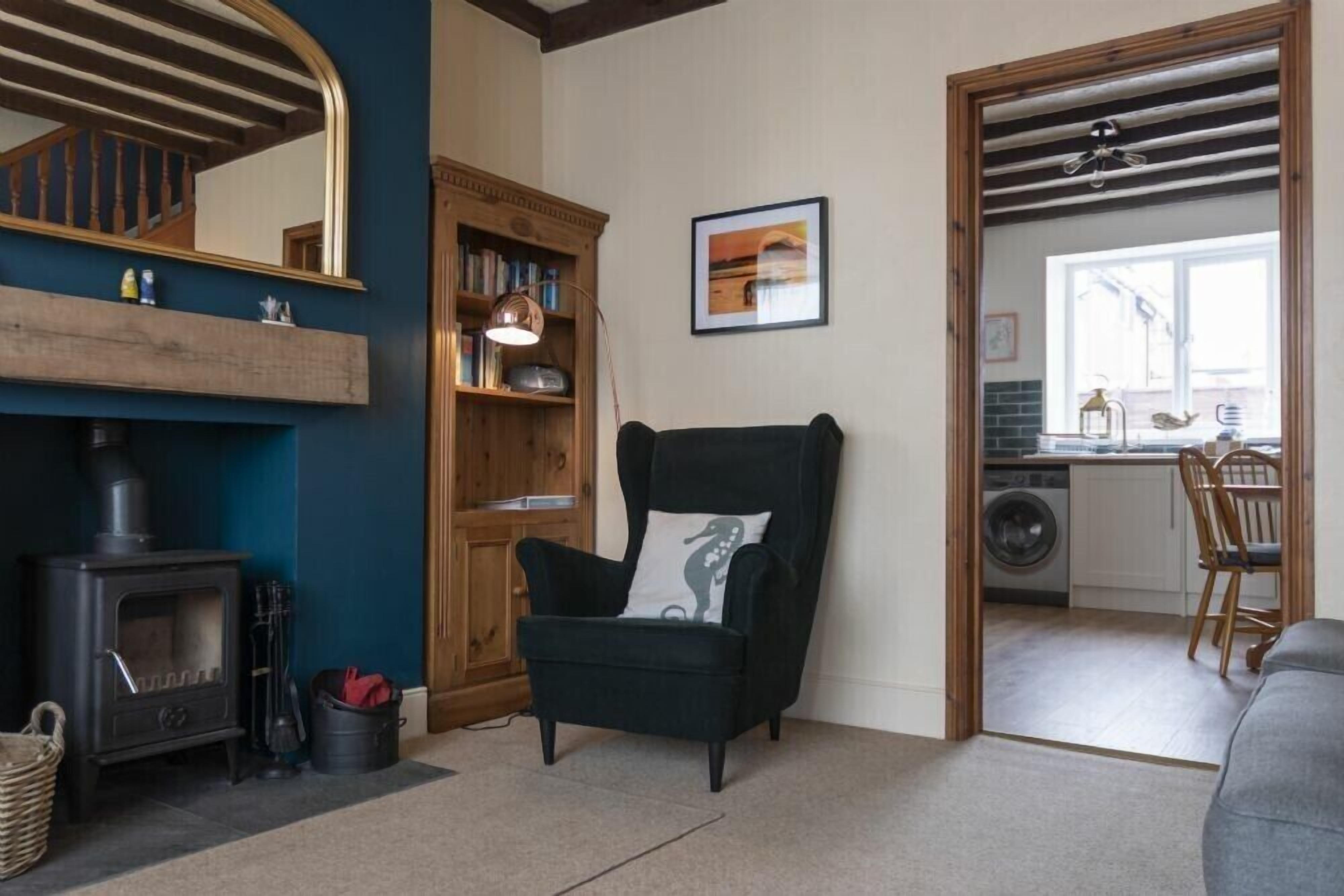 Uma sala de estar aconchegante com lareira, estante de livros, poltrona confortável e vista para a cozinha.