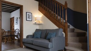 Una sala de estar con un sofá gris, una escalera de madera y un comedor con sillas y una mesa de madera.