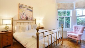 A bedroom with a bed, bedside tables, a window, and a pink armchair.