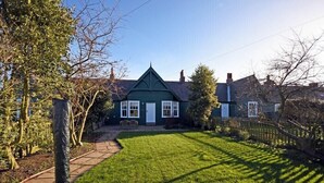 A green house with a white door, a paved driveway, and a well-maintained lawn.