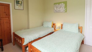 A bedroom with two single beds, a wooden wardrobe, and a door. - No2 Budle Bay Cottage (Bamburgh)