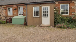 A stone building with a green door, a window, and a small garden with pink flowers. - No2 Budle Bay Cottage (Bamburgh)