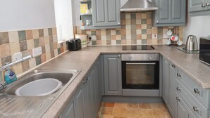 A kitchen with grey cabinets, a stainless steel sink, a built-in oven, and a tiled backsplash. - No2 Budle Bay Cottage (Bamburgh)