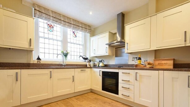 A kitchen with white cabinets, a stainless steel range hood, a built-in oven, and a window with a stained glass design. - Sunnybrae (Alnwick)
