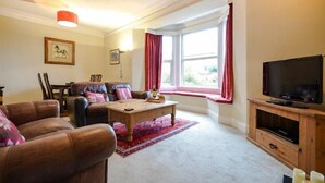 A living room with a sofa set, a coffee table, a TV, and a window with curtains. - Sunnybrae (Alnwick)