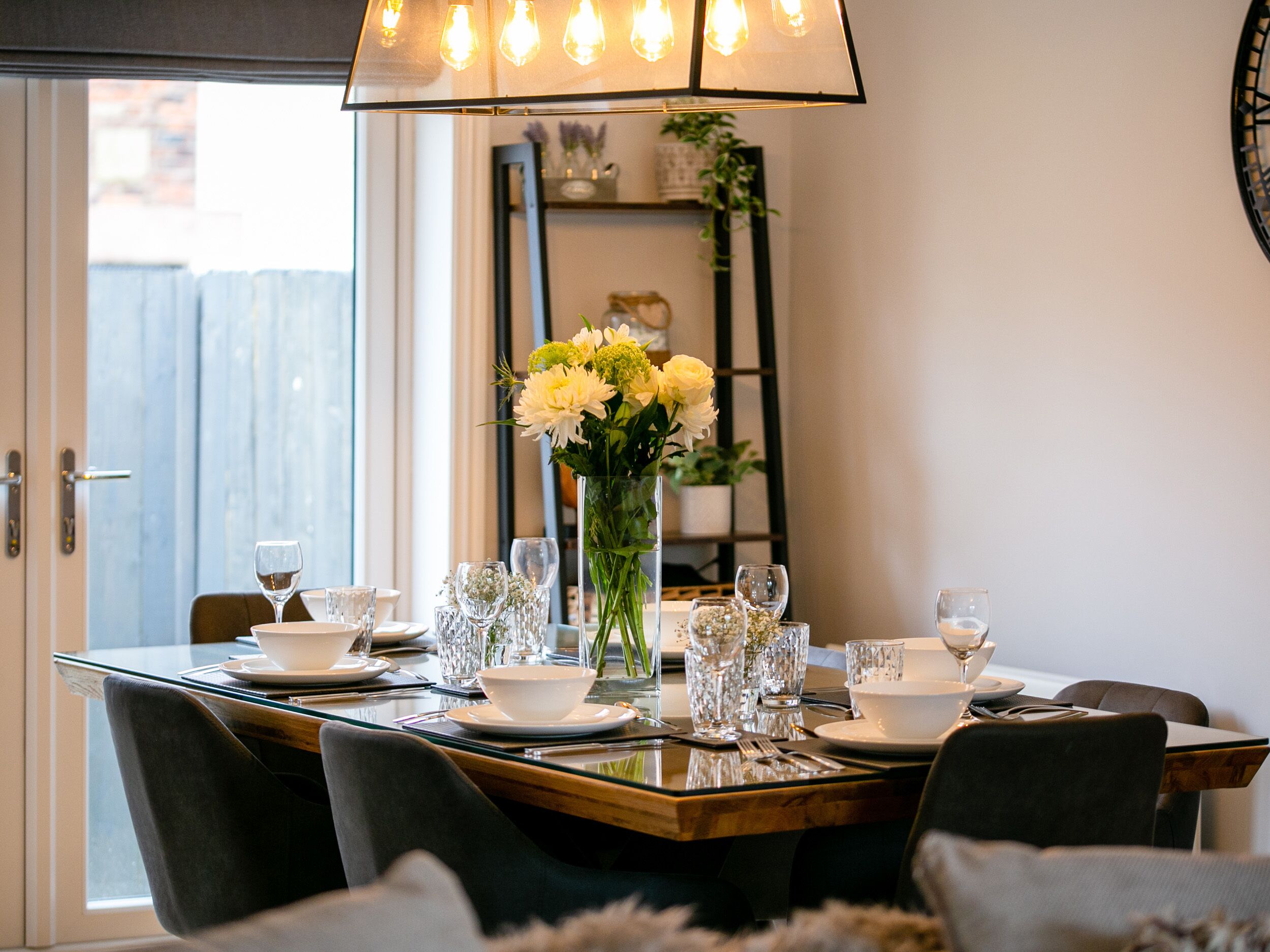 A dining table set for six with a vase of flowers, clear glassware, and plates.