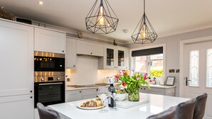 Une cuisine moderne avec des meubles blancs, des appareils en acier inoxydable et une table à manger blanche accompagnée de deux chaises.