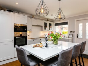 A modern kitchen with white cabinetry, stainless steel appliances, and a white dining table with two chairs.
