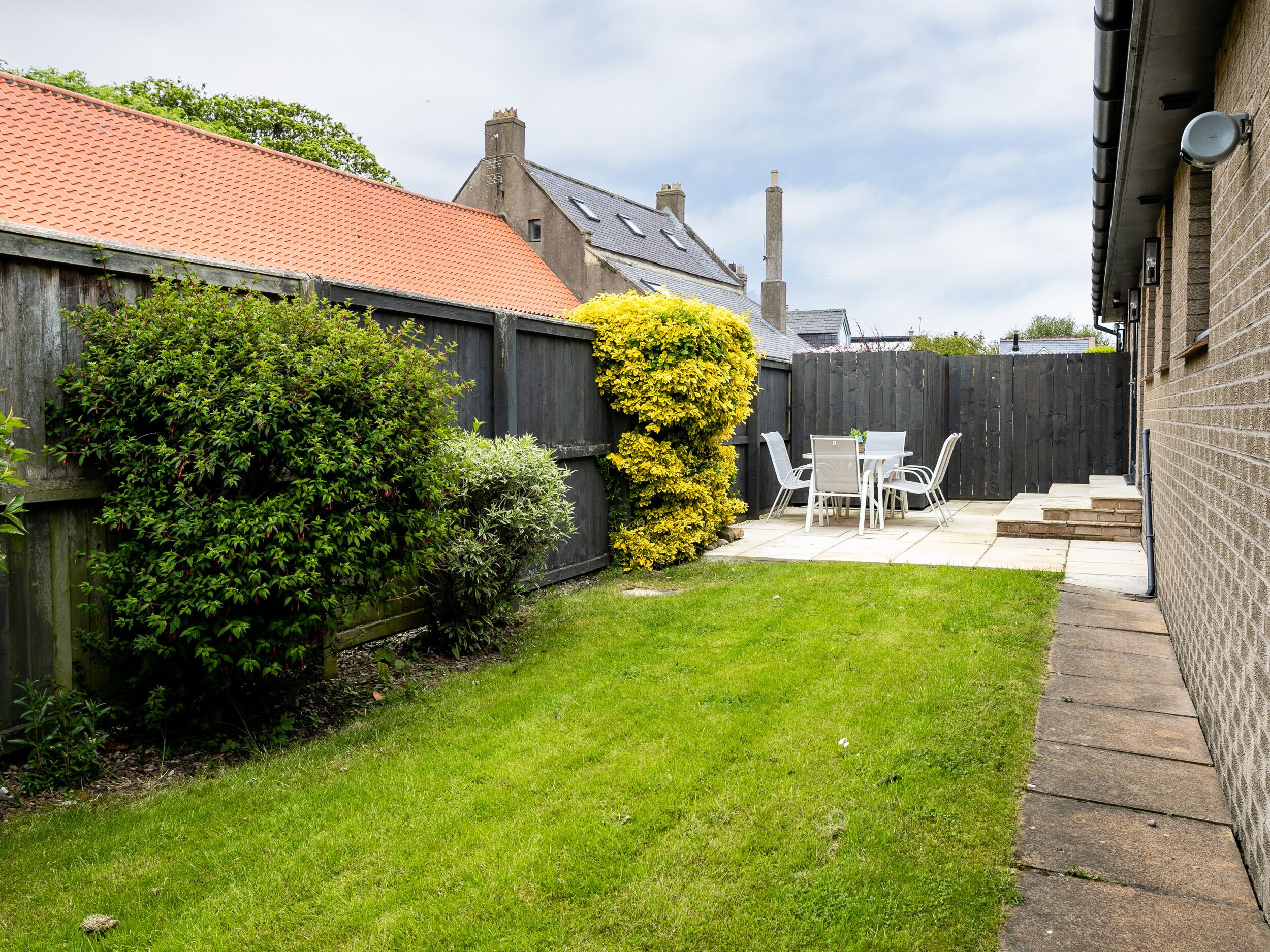 A backyard with a patio, a wooden fence, and a hedge.