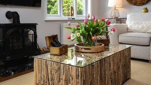 Un salon avec une table basse en verre, une cheminée, un canapé et une fenêtre donnant sur un paysage verdoyant.