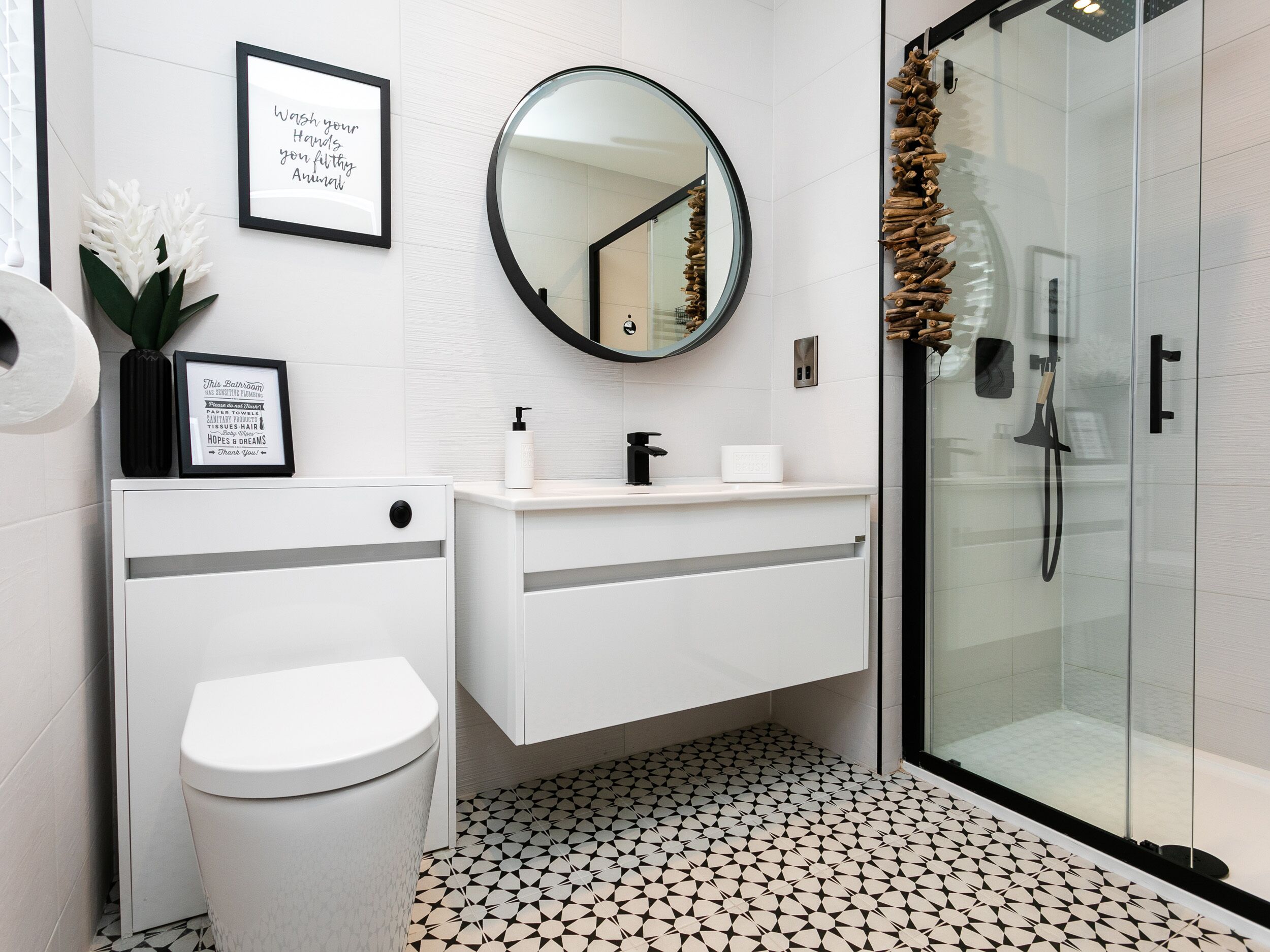 A modern bathroom with a toilet, sink, and shower. There are framed signs on the wall and a mirror above the sink.
