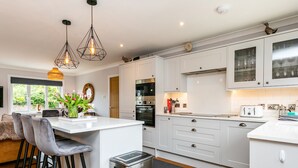 Une cuisine moderne avec des meubles blancs, un îlot central doté de tabourets de bar, des appareils en acier inoxydable et un éclairage suspendu.